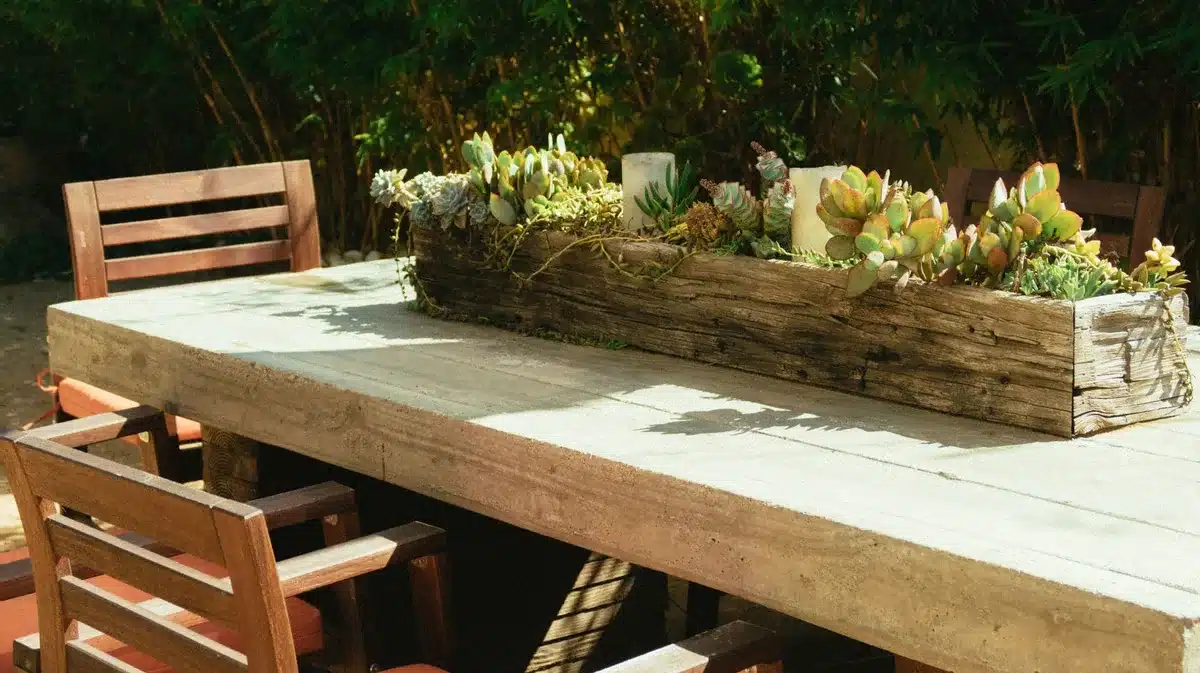 Two deck storage boxes on a residential deck with patio furniture and garden items in the background
