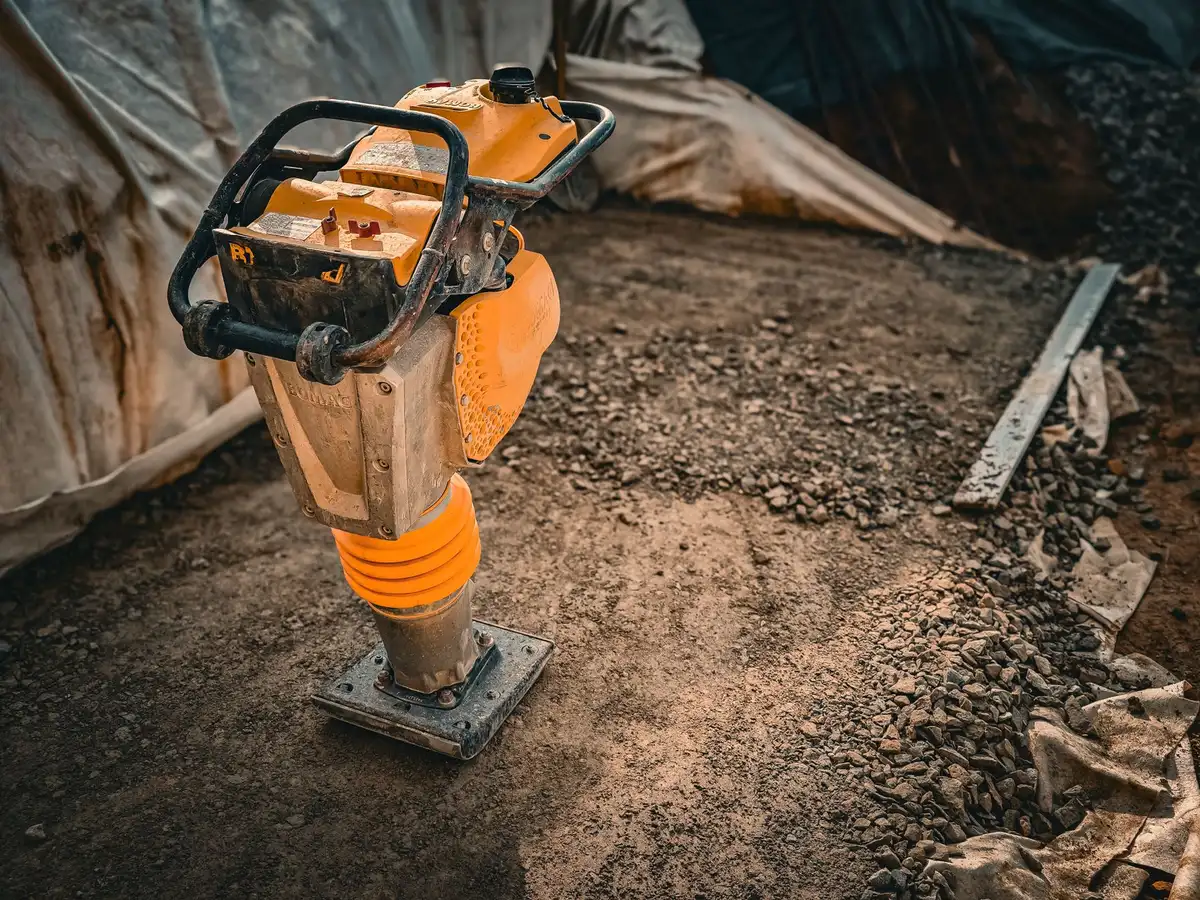 Worker compacting and leveling gravel driveway surface with proper technique