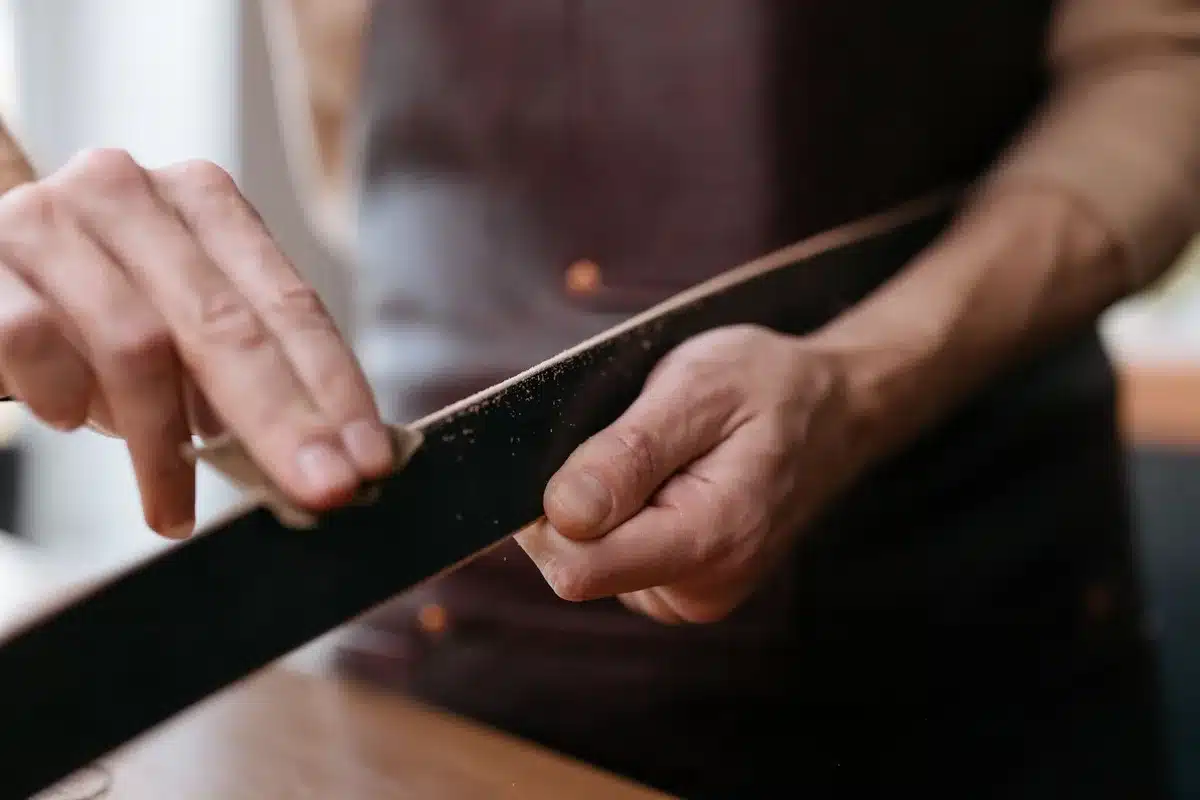 Orbital sander smoothing wooden surface, with fine-grit sandpaper and finish products nearby