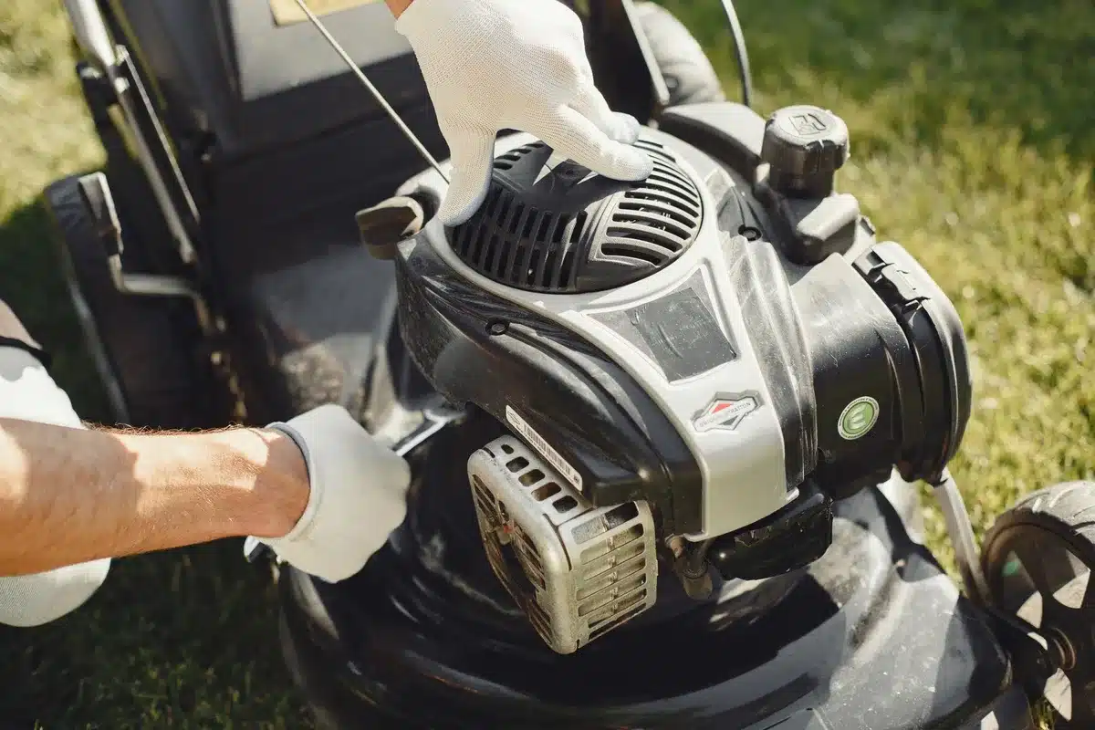 Hands pushing a manual reel mower across green lawn in bright daylight