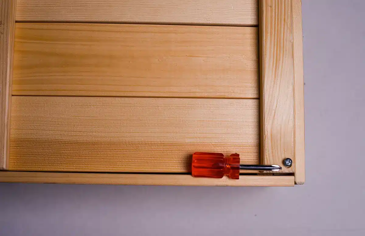 Hands assembling wooden furniture pieces with tools and fasteners on a work surface