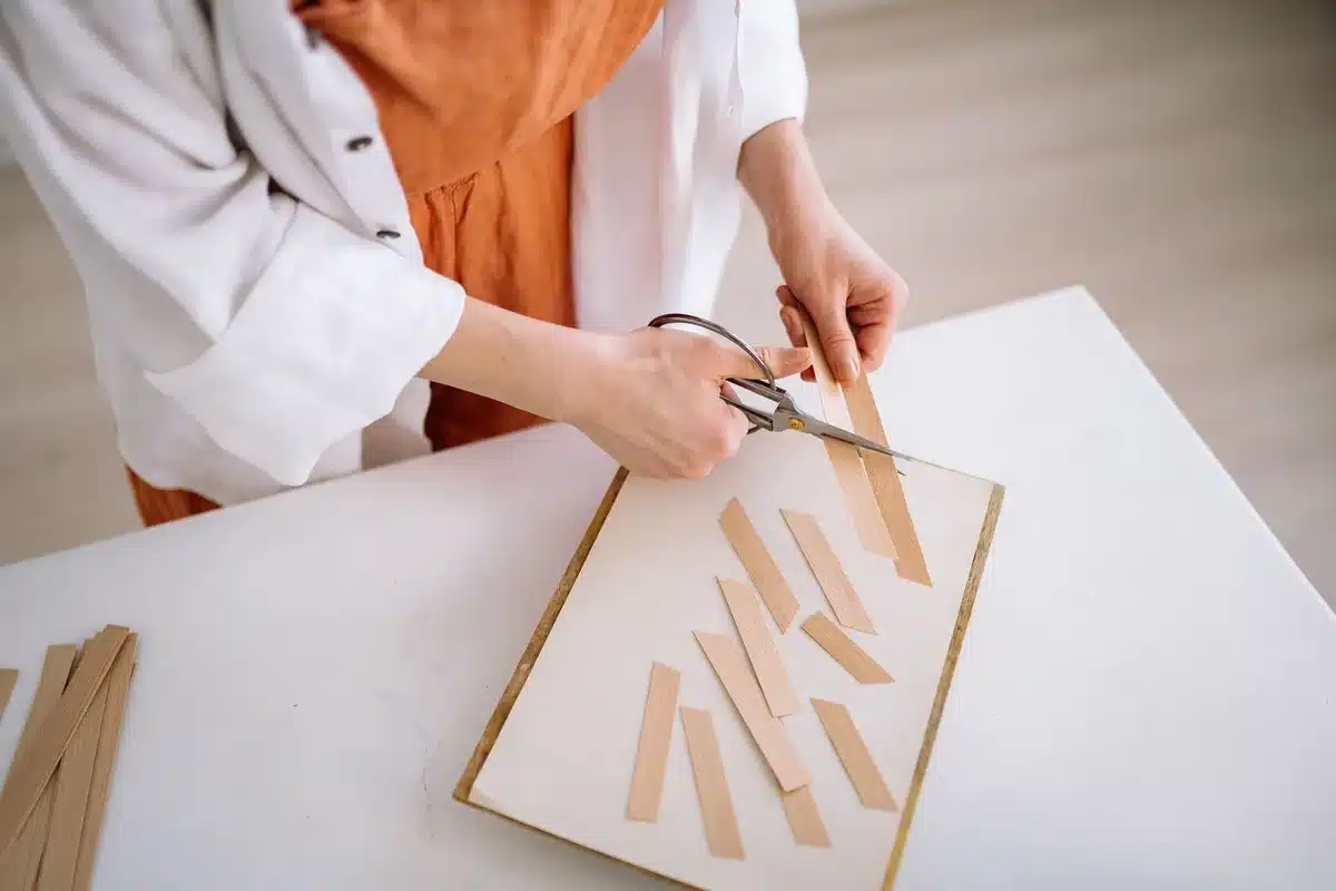 Hands cutting a plastic milk jug with scissors on a bathroom counter with craft supplies nearby