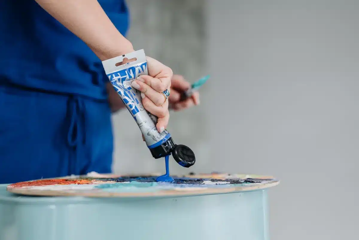 Hands applying blue acrylic paint to the interior of an old frying pan with a brush