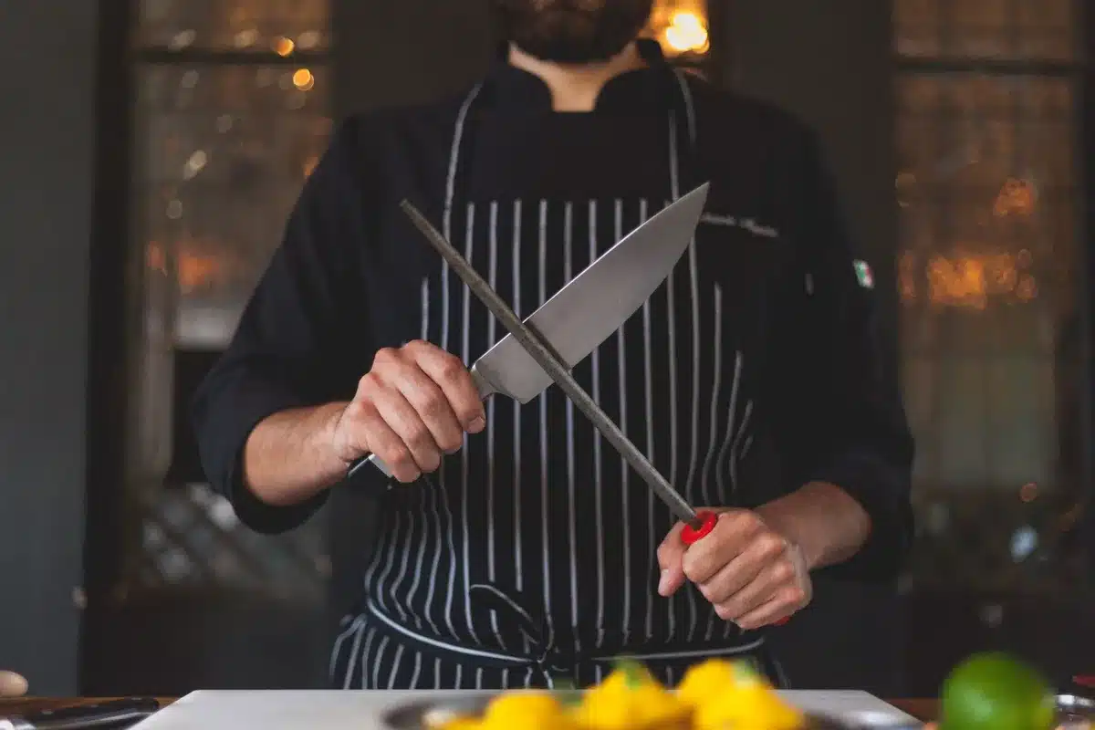 Hands guiding a kitchen knife through a rolling sharpener on a stable work surface