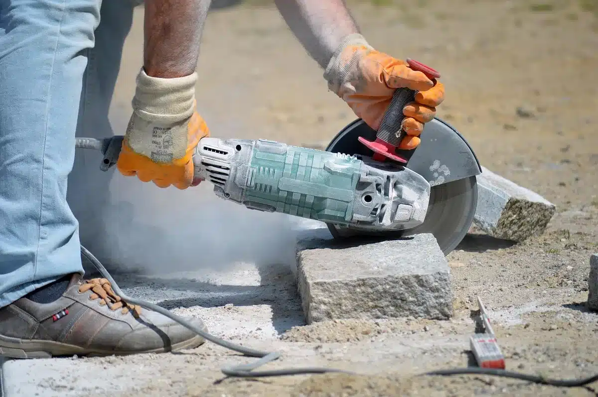 Cordless angle grinder in use on metal workpiece with safety equipment visible