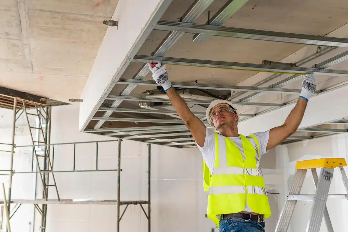 Professional installer attaching smooth drywall panels to cover an existing textured ceiling.