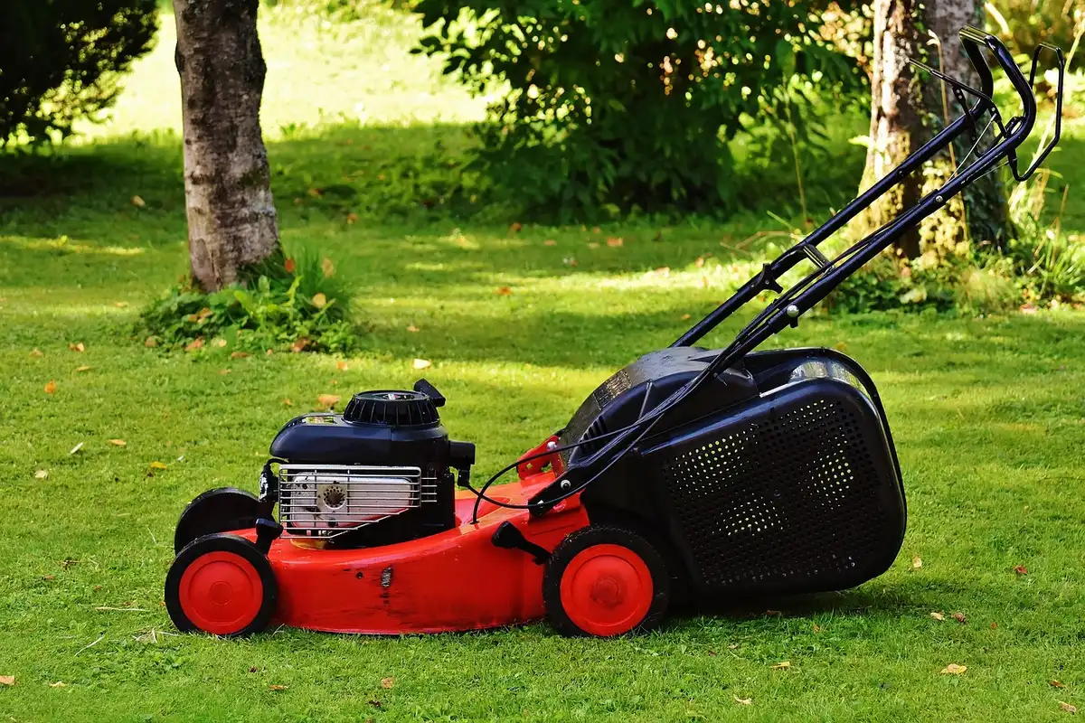 Gloved hands holding a mower blade above a freshly cut lawn