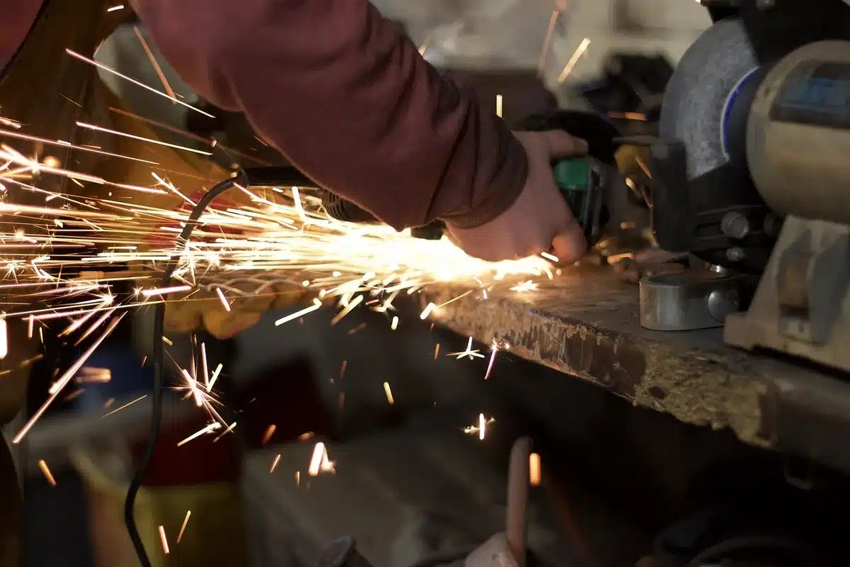 Hands with gloves holding a tool to a spinning wire wheel on a bench grinder