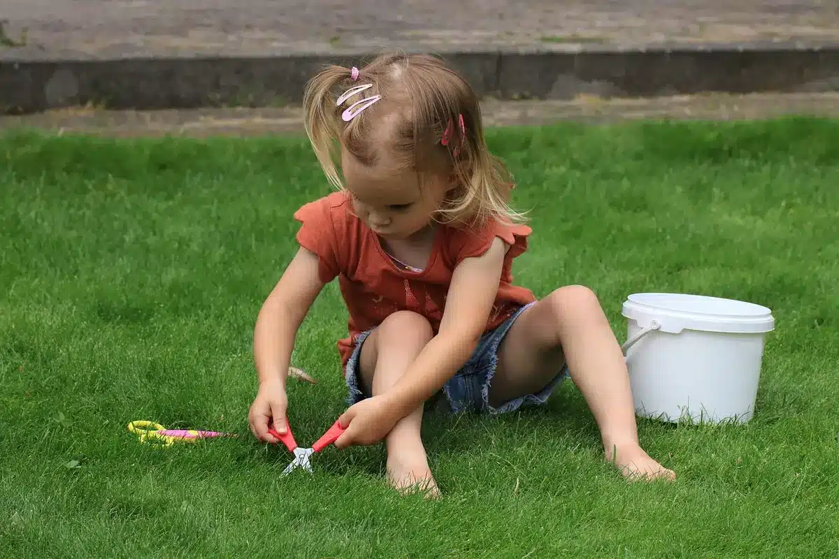 Homeowner using a spreader on a green lawn with a soil test kit on a table