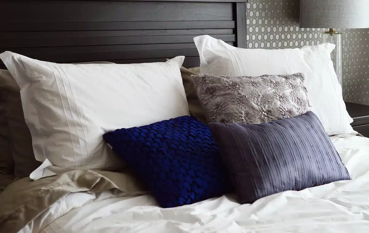 Bedroom with driftwood wall art above bed, blue-gray wall and linen bedding