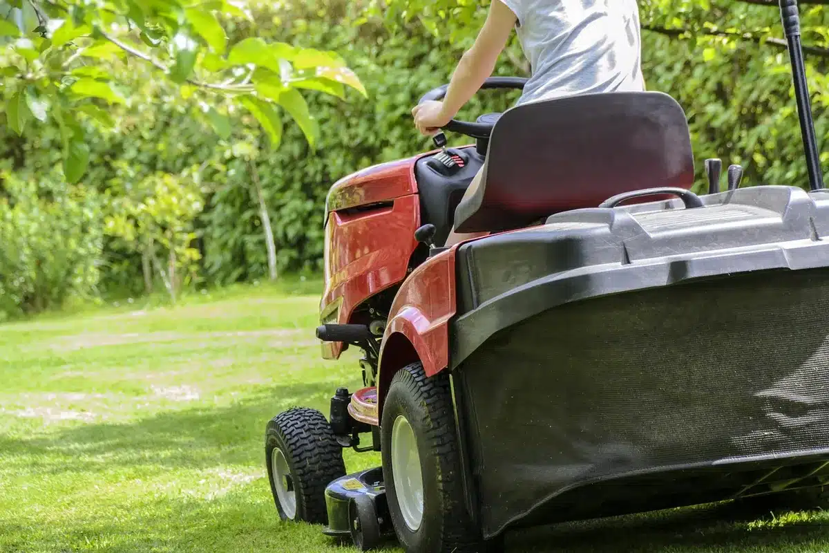 Person wearing gloves using a wire wheel on a mower deck in daylight